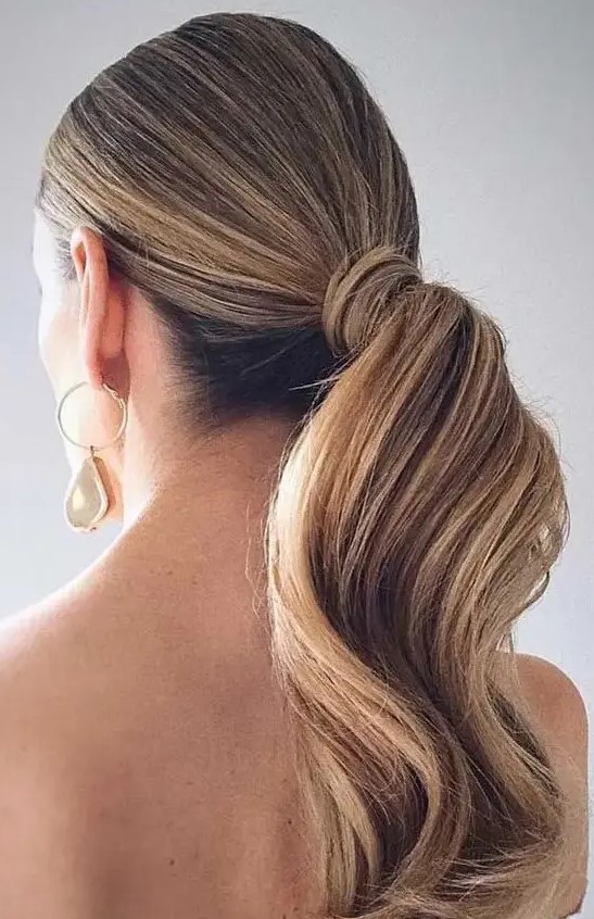 an elegant and refined low wavy ponytail with a sleek top is a stylish idea for a modern or minimalist bride, wrap the ponytail with your hair