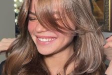 an elegant and shiny brown butterfly haircut with curtain bangs and a bit of waves to make it more dimensional