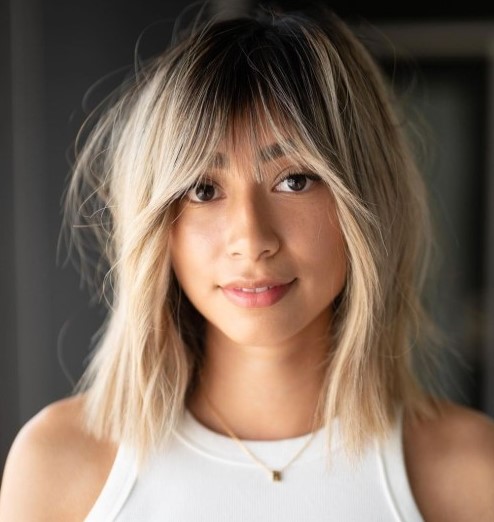 Blonde hair with a darker root and texture plus outgrown looking wispy bangs for a delicate touch