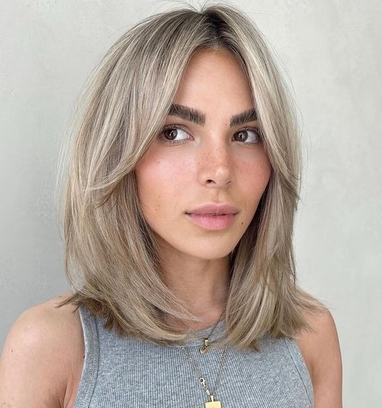cold blonde medium length hair with a darker root and curtain bangs is a stylish and chic idea