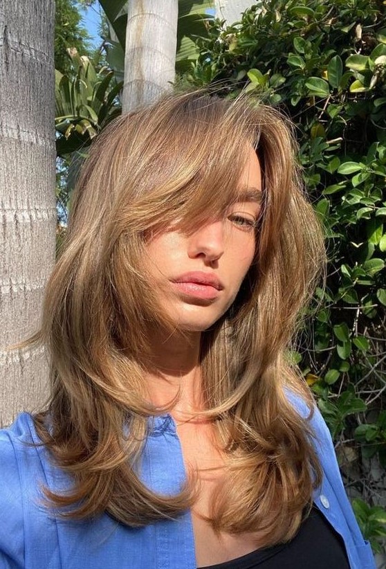 long bronde hair with a butterfly haircut, with caramel highlights and face-framing locks and curved ends