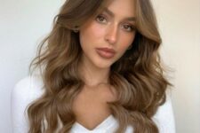 long wavy brown hair with caramel balayage and soft curtain bangs that frame the face and accent the eyes
