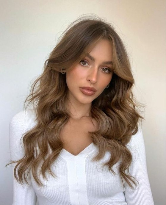 long wavy brown hair with caramel balayage and soft curtain bangs that frame the face and accent the eyes