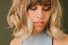 medium-length blonde hair with a darker root and waves plus wispy bangs for an effortlessly chic and cool look