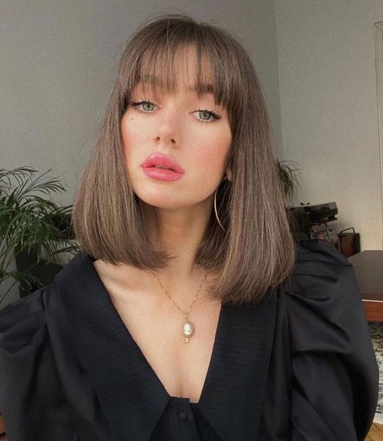 Medium length brunette hair with wispy bangs and rounded ends looks doll like and chic