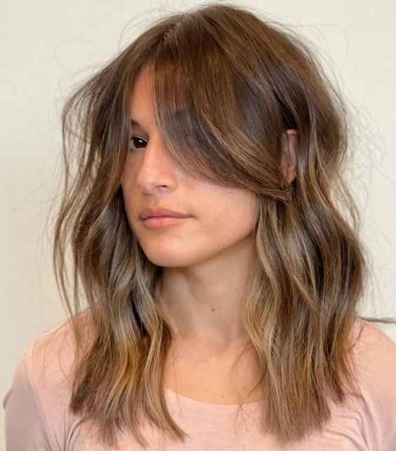 Medium length brunette haur with long curtain bangs, a slight wavy touch and an ombre effect