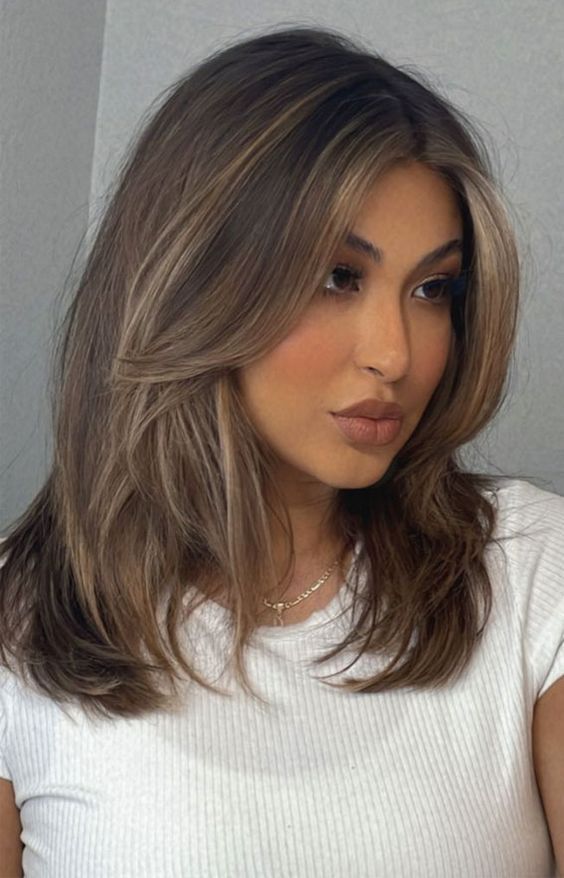 Medium length dark brunette hair with long curtain bangs and blonde contouring is chic