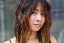 medium-length shaggy hair in dark shades and with caramel balayage, with wispy bangs to accent the eyes even more