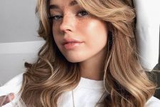 medium wavy hair with curtain bangs and blonde contouring plus some volume is a stylish and relaxed idea