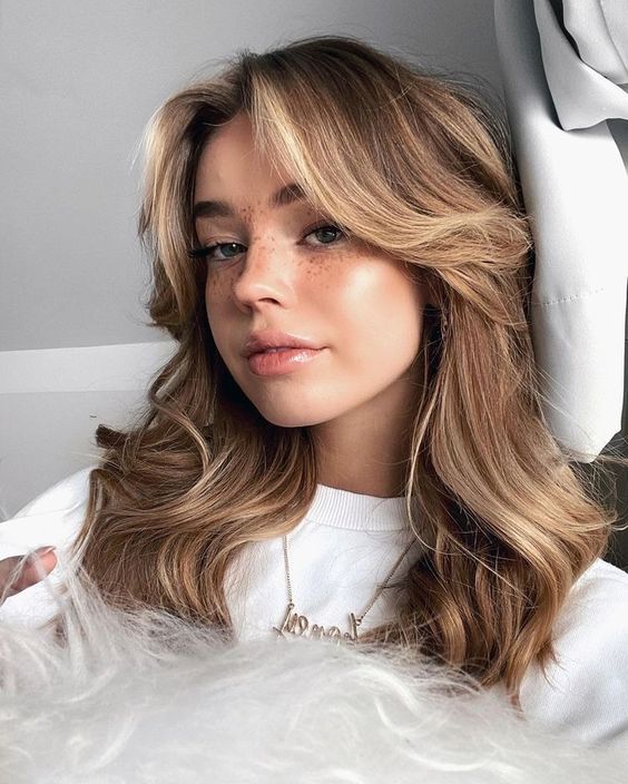 medium wavy hair with curtain bangs and blonde contouring plus some volume is a stylish and relaxed idea