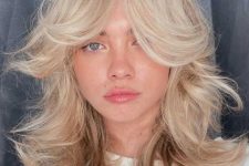 messy and voluminous blonde shoulder-length hair with curtain bangs and natural wavy texture