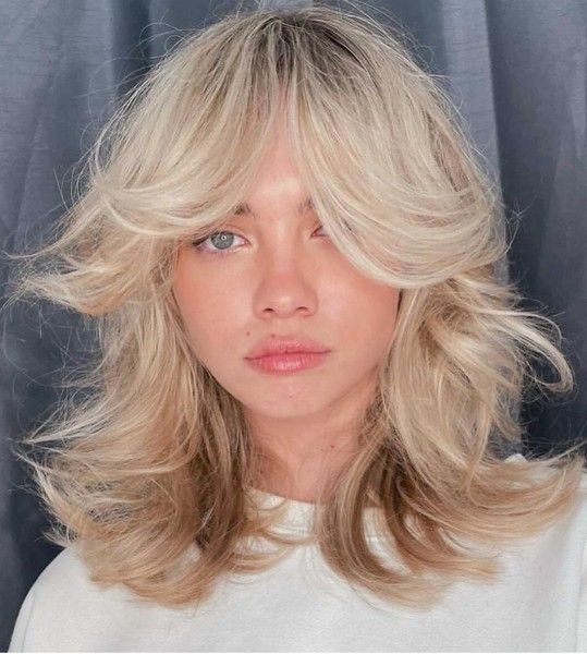 Messy and voluminous blonde shoulder length hair with curtain bangs and natural wavy texture