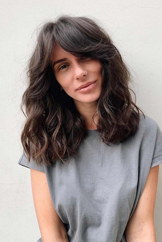 pretty messy and voluminous dark brunette hair with curtain bangs and waves is an effortlessly chic idea