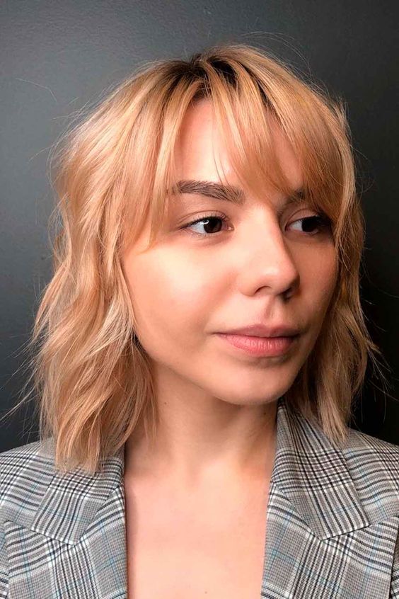pretty peachy wavy medium-length hair with a darker root and wispy bangs is a fresh and cool idea that catches an eye with color