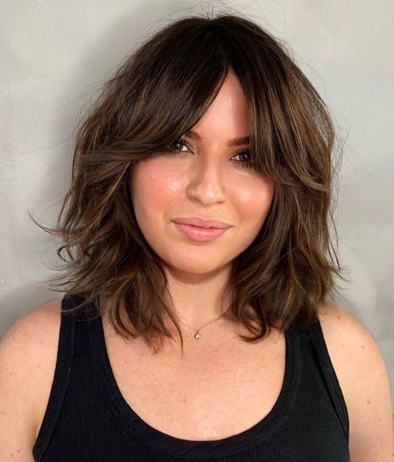 a beautiful dark brunette long bob with waves and bottleneck bangs features dimension and is ultimately cute