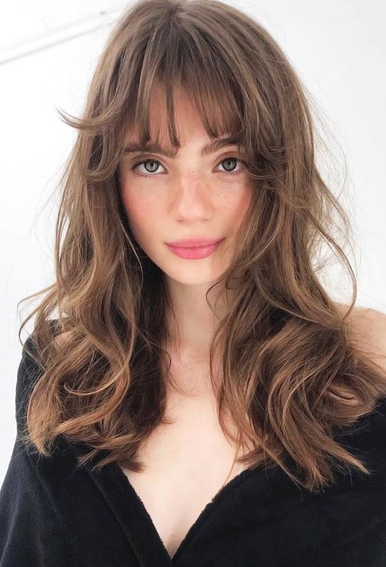 a beautiful long brunette butterfly haircut with messy waves and wispy bangs is a cool and relaxed idea to rock right now