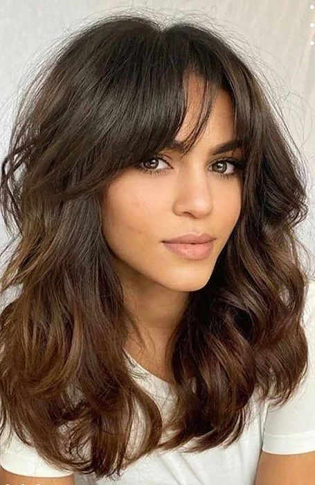 a beautiful medium butterfly haircut with wispy bangs and caramel balayage is a gorgeous idea for thick hair, it looks adorable