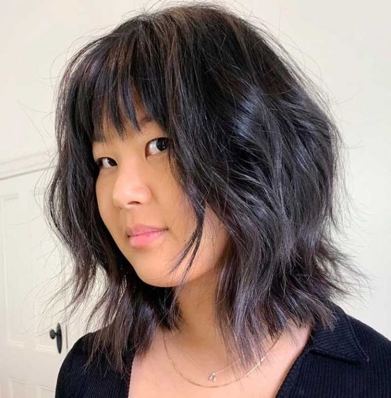 a black medium wavy wolf cut with blunt bangs and shiny hair is a chic and cool idea to rock