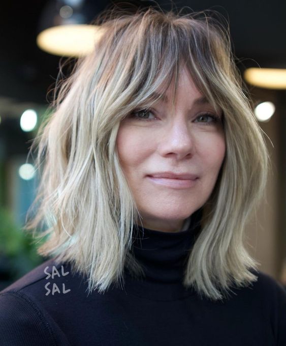 a blonde blunt bob with a darker root and bottleneck bangs plus messy waves is a chic and cool idea