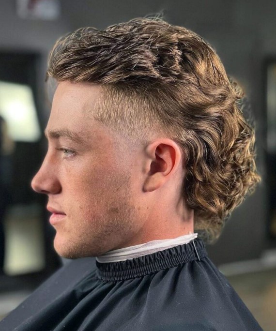 A Blonde Curly Back Mullet With A Touch Of Fade And A Top Pushed Back Is A Very Bold Style Statement 