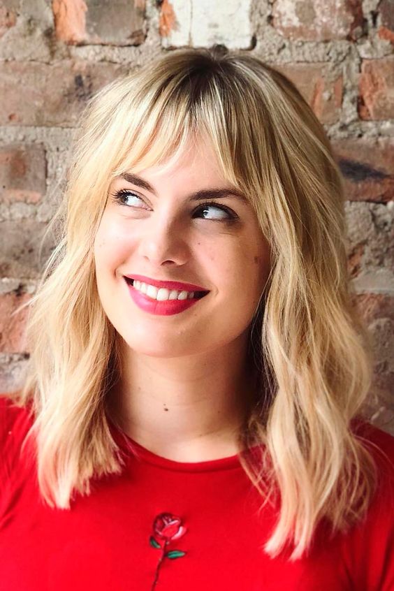 A blonde medium length haircut with bottleneck bangs and messy waves is a chic and cool solution