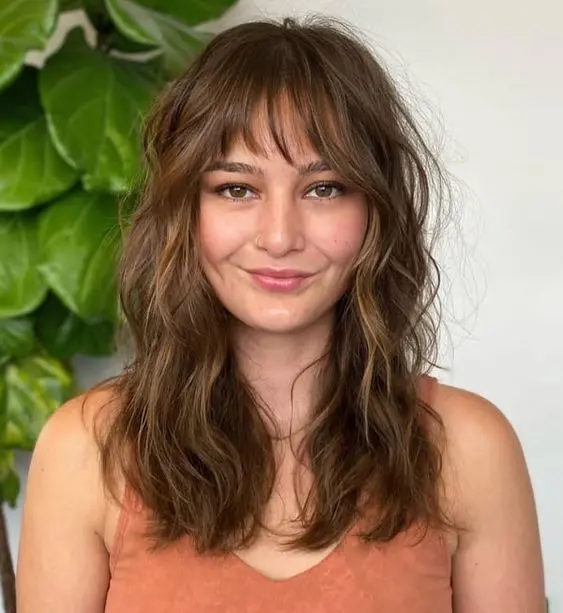 a brown long wolf haircut with wispy bangs, caramel balayage and soft waves to make the cut look cuter