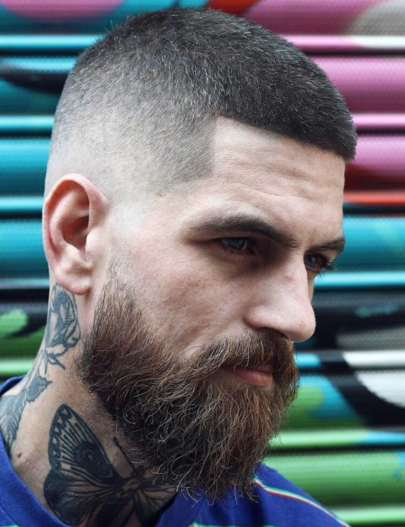 a buzzed top with an angled line up and a fine skin fade that is balanced with a long and thick beard
