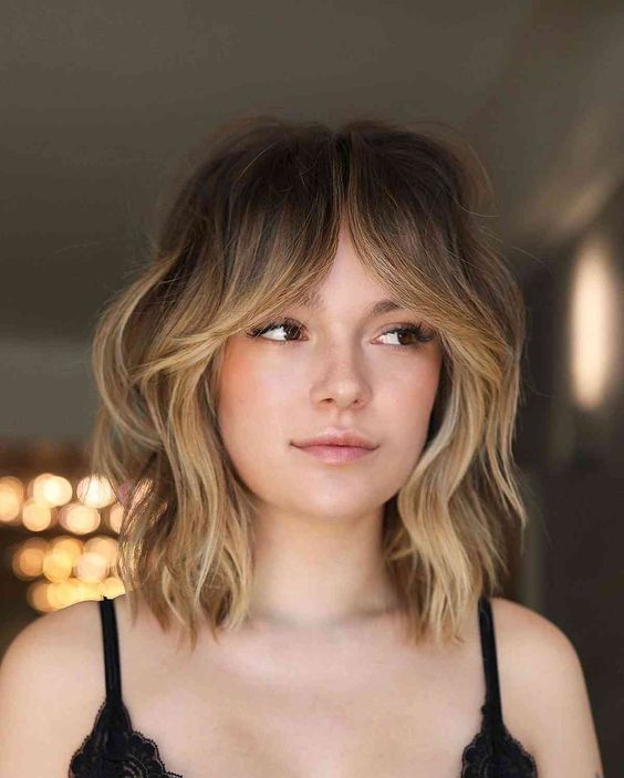 a chic medium wolf cut with waves, blonde balayage and bottleneck bangs is a catchy idea