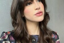 a dark brunette long butterfly haircut with wispy to bottleneck bangs and waves is a cool and girlish idea to try