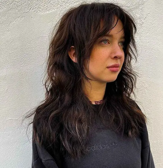 a dark brunette long wolf haircut with curtain bangs and face-framing layers and messy waves is cool