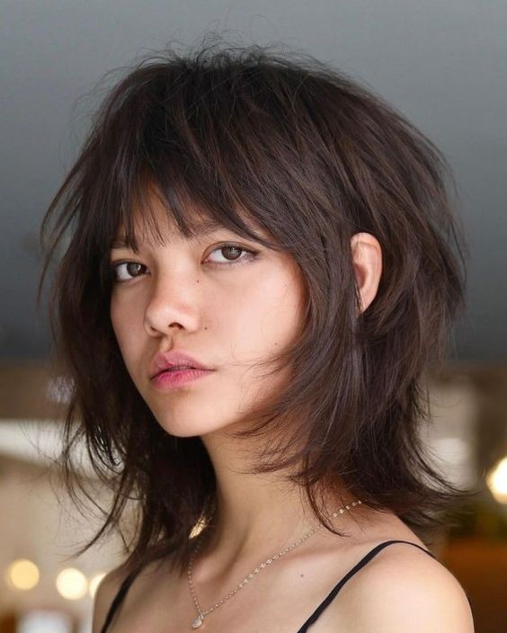 A dark brunette medium wolf cut with wispy bangs and messy volume is a super cool idea for medium length hair