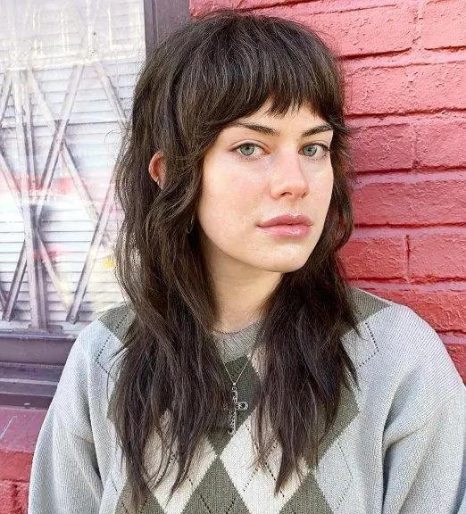 a dark brunette wolf haircut with blunt bangs and waves down is a cool and chic idea to rock right now