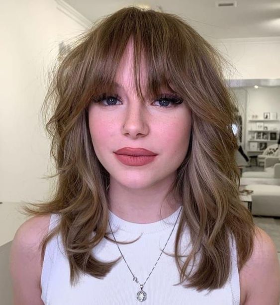 a light brunette medium wolf cut with bottleneck bangs and waves looks very chic, catchy and romantic