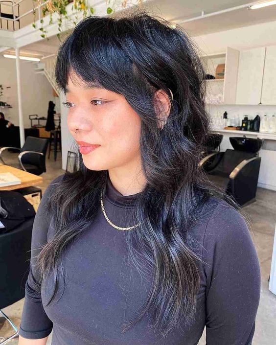 a long black wolf cut with bottleneck bangs and wavy hair with a bit of volume is a catchy solution to try
