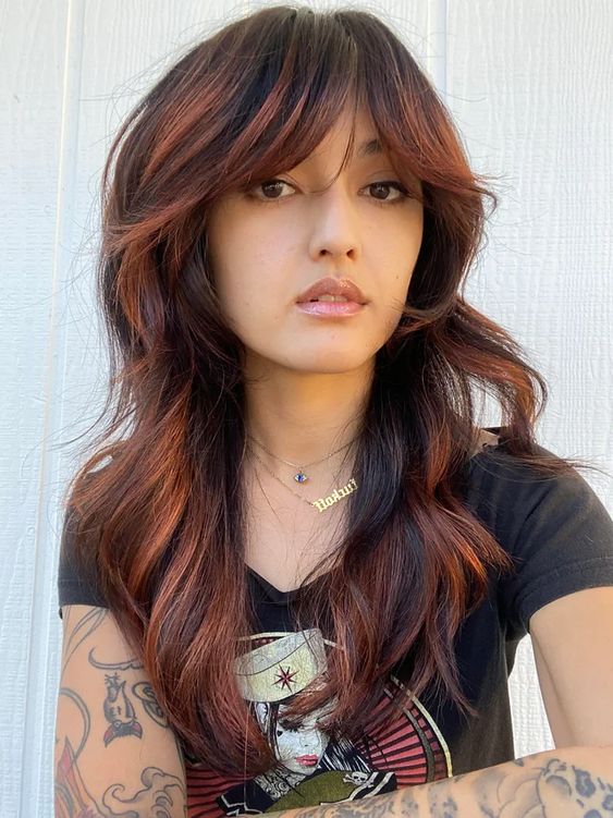 a long black wolf haircut with ginger balayage, bottleneck bangs and waves is a bold and eye-catching idea