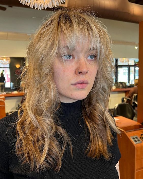 a long blonde wavy wolf cut with outgrown wispy bangs is a catchy and soft idea, just add volume to it