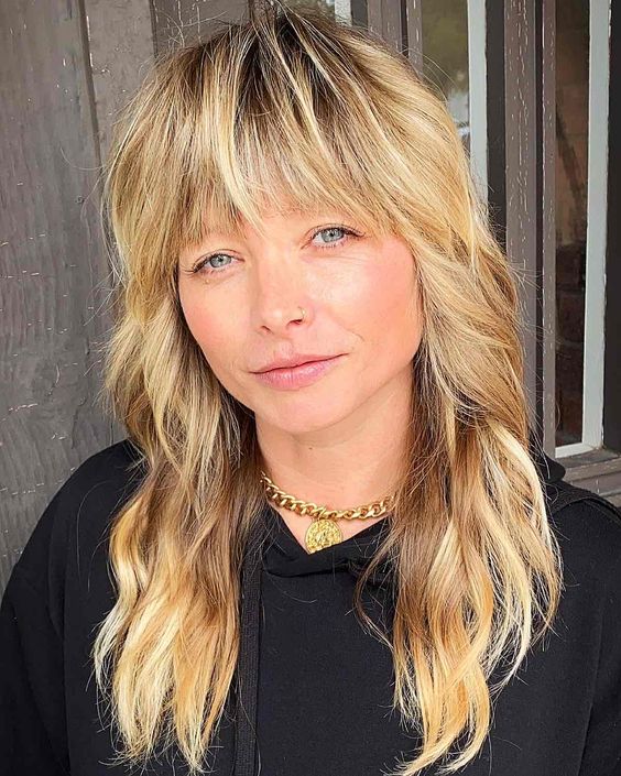 a long blonde wolf cut with outgrown blunt bangs and wavy volume is a stylish solution to try