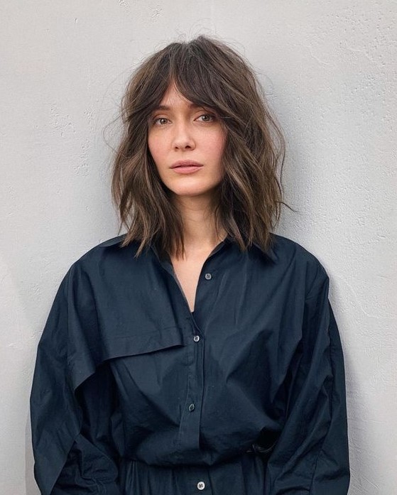 a long brown bob with slight highlights, messy waves and bottleneck bangs is a trendy solution to rock now