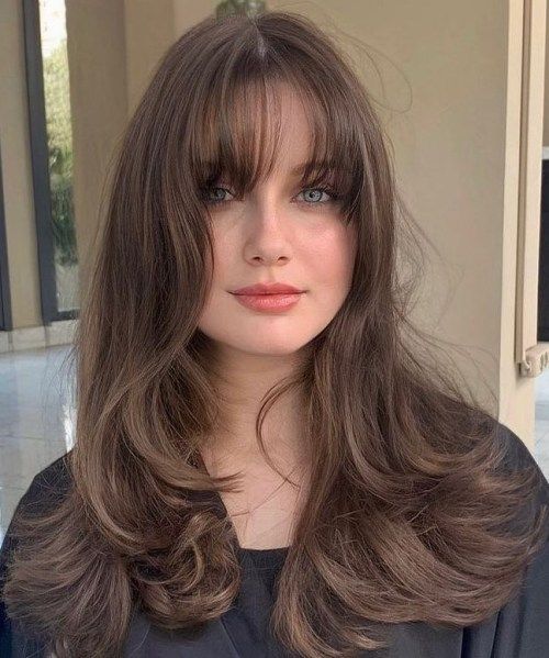 A long brunette wolf cut with bottleneck and wispy bangs and waves looks luxurious and very eye catching