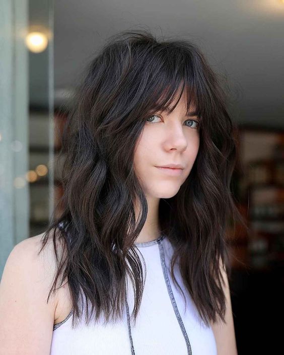 a long dark brown wolf haircut with wispy bangs and messy waves is a chic and cool idea with a lot of volume
