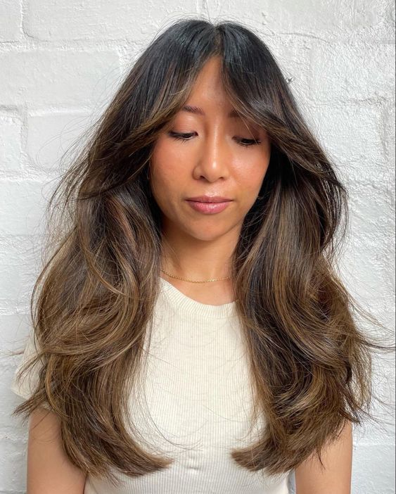 a long dark brunette haircut with bottleneck bangs, dimension and waves plus caramel balayage
