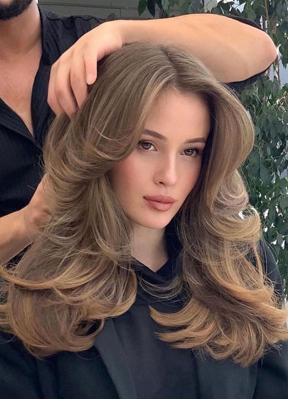 a lovely bronde butterfly haircut with long curtain bangs and curled ends is a gorgeous solution