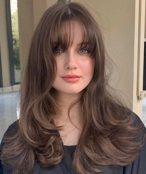 a lovely brunette butterfly haircut with waves and wispy bangs is a cool and chic idea and it shows off your locks