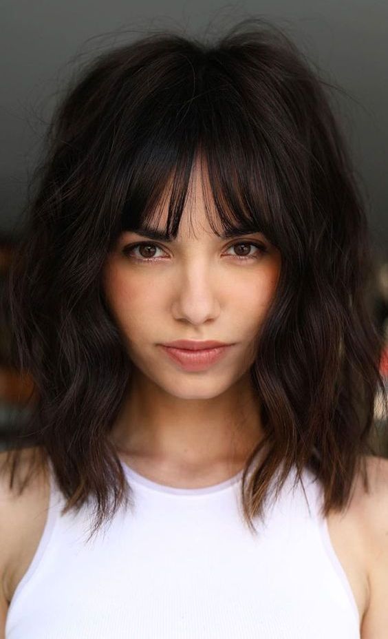 a lovely dark brunette shaggy long bob with bottleneck bangs and a lot of volume plus a bit of waves