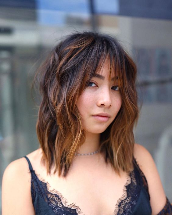 a medium black wolf cut with wispy bangs and caramel balayage and messy waves is a catchy and bold idea