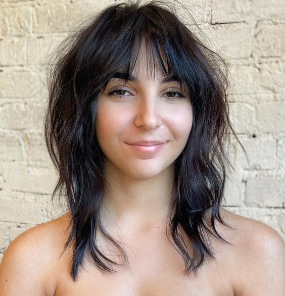 a medium dark brown wolf haircut with wispy bangs and messy waves looks very up-to-date and fresh