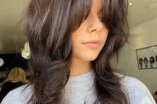 a medium dark brunette wolf cut with bottleneck bangs and a lot of volume and waves is a very chic and cool idea