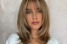 a medium-length blonde butterfly haircut with wispy bangs and curved ends is a delicate and girlish solution