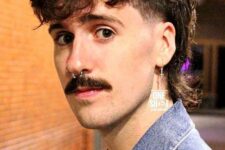 a messy tousled mullet with curly fringe and curls on the back, with a lot of volume and a moustache create a retro look