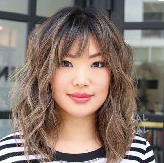 a shaggy long bob with caramel highlights and wispy and bottleneck bangs looks super cute and chic